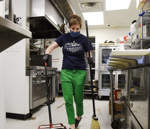 Woman sweeping floor in restaurant kitchen.