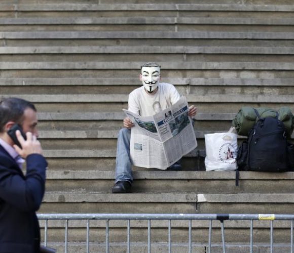 Man in mask sitting on steps with newspaper in hand.